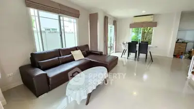 Spacious living room with modern brown leather sofa and dining area, large windows, and bright ambiance.