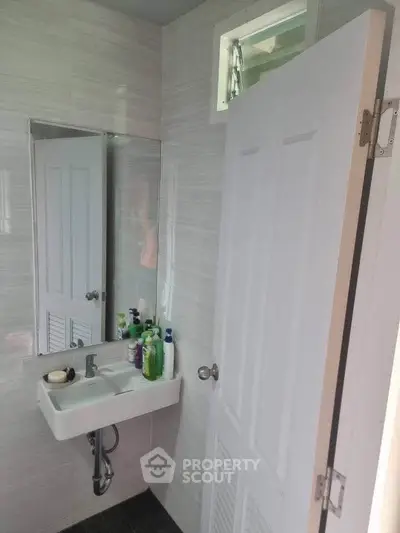 Compact bathroom with modern sink and mirror, featuring sleek white door and tiled walls.