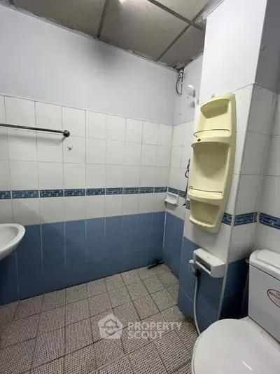 Compact bathroom with tiled walls and floor, featuring a toilet and wall-mounted shower caddy.