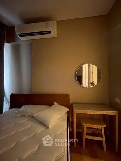 Cozy bedroom with air conditioning and minimalist decor, featuring a bed, mirror, and small desk with stool.