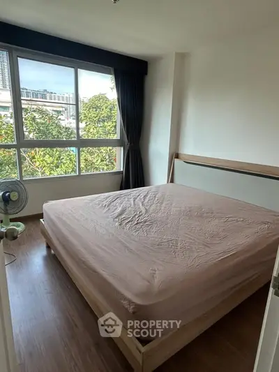 Bright bedroom with large window and wooden flooring, offering a serene view of greenery.