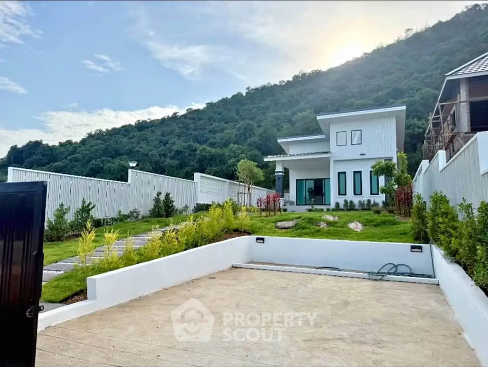 Modern hillside home with lush garden and spacious driveway, offering serene mountain views.
