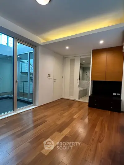 Spacious modern living room with wooden flooring and large glass doors leading to a balcony.