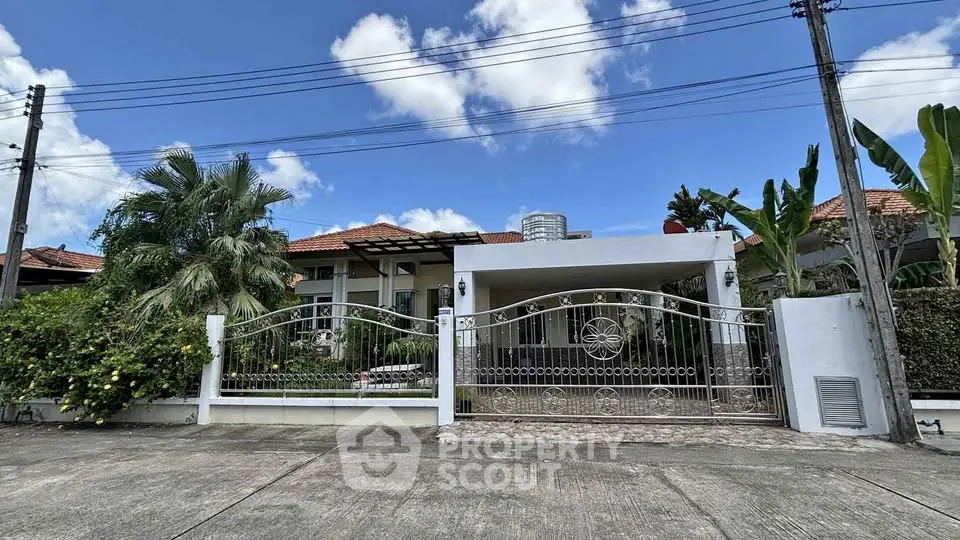 Charming suburban house with gated entrance and lush greenery under a clear blue sky.