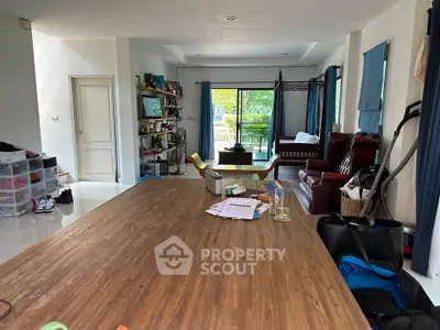 Spacious living room with wooden table and large windows opening to a balcony with lush greenery view.
