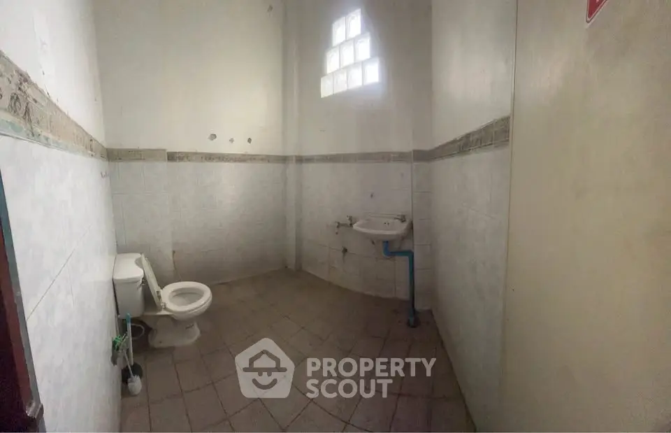 Spacious bathroom with tiled walls and floor, featuring a toilet and sink, ideal for renovation.