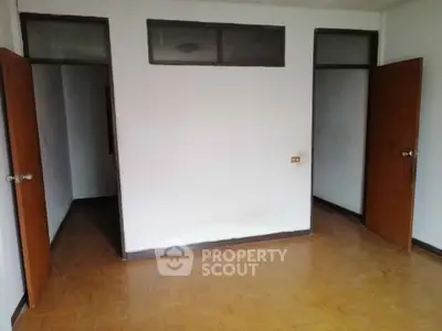 Spacious room with wooden flooring and two doorways, ideal for versatile use.