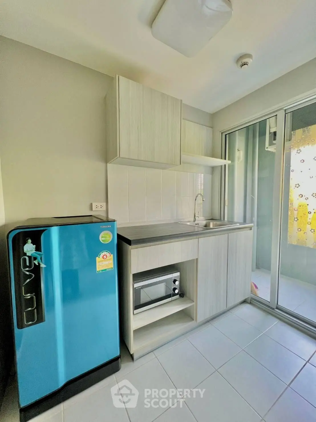 Modern compact kitchen with blue fridge and microwave, bright natural light
