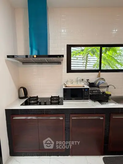 Modern kitchen with gas stove, microwave, and sleek cabinetry, featuring a window view of lush greenery.