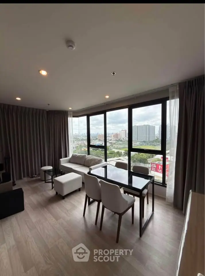 Spacious living room with large windows offering stunning city views, modern furniture, and elegant decor.