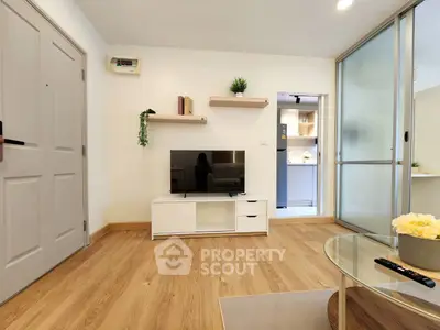 Modern living room with wooden flooring, TV unit, and open kitchen view.