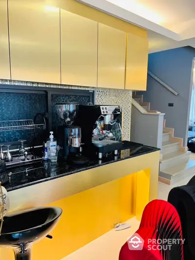 Chic modern kitchen with bold yellow cabinets and sleek black countertops, complemented by stylish mosaic backsplash and premium stainless steel appliances, adjacent to an elegant staircase.