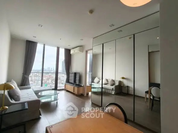 Spacious modern living room with floor-to-ceiling windows and city view, featuring elegant furniture and mirrored wardrobe.