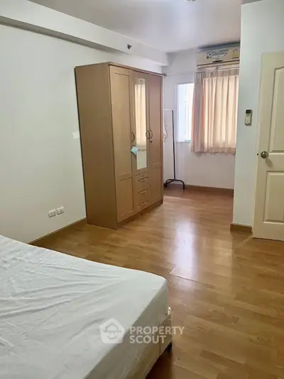 Spacious bedroom with wooden flooring and ample natural light, featuring a wardrobe and air conditioning.