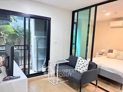 Modern apartment with cozy living area and bedroom, featuring sleek glass partitions and natural light.