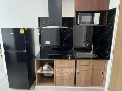 Modern kitchen with sleek black backsplash, microwave, and refrigerator in stylish apartment.