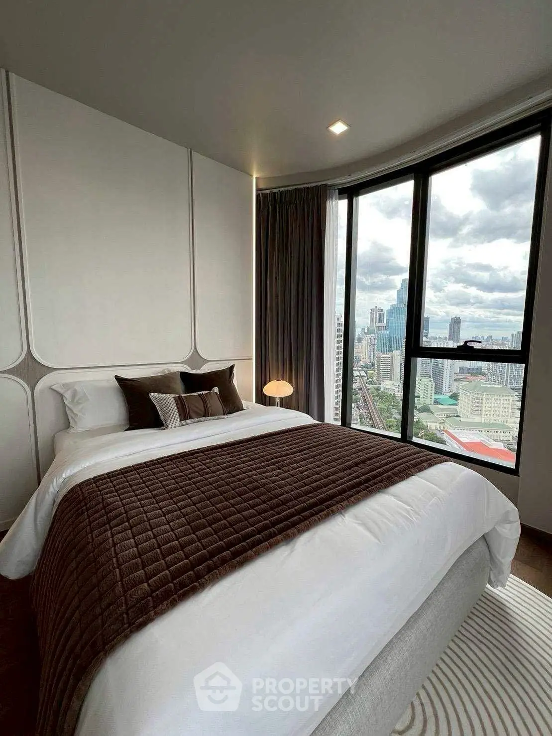 Luxurious bedroom with stunning city view from large windows, elegant decor and cozy ambiance.