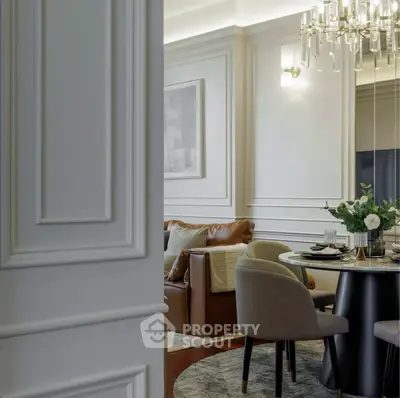 Elegant living room with modern chandelier and stylish dining area, featuring a cozy leather sofa and chic decor.