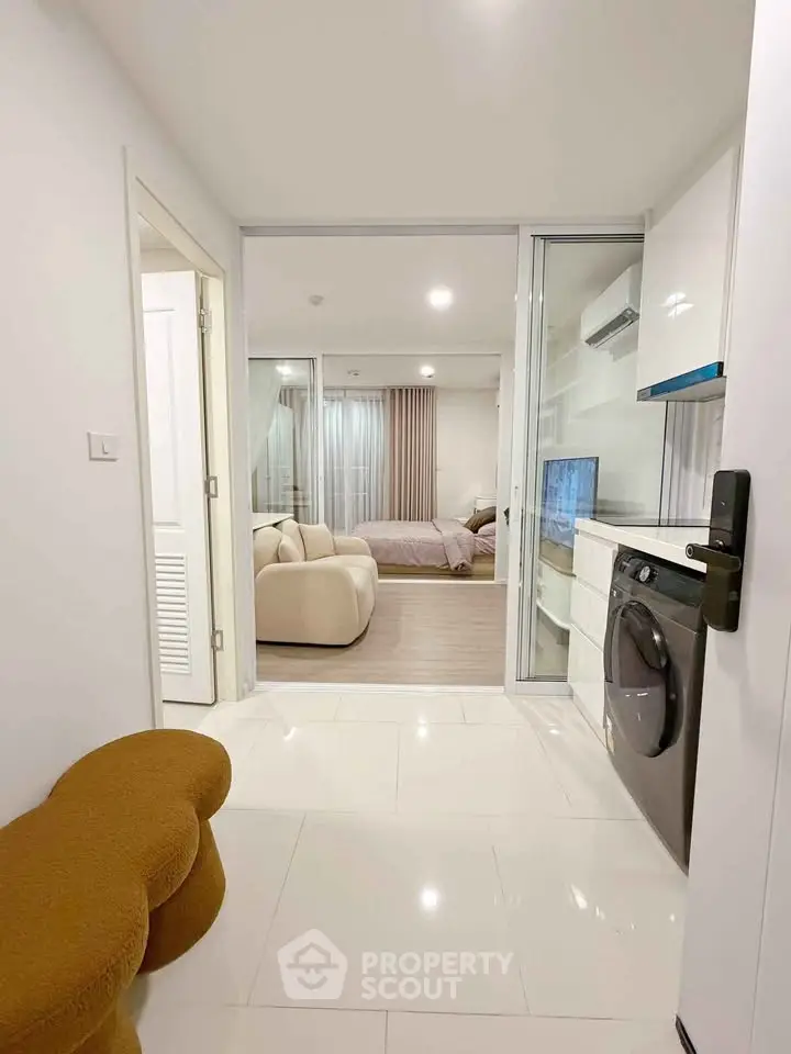 Modern apartment interior with open layout, featuring cozy living area and compact kitchen with washing machine.