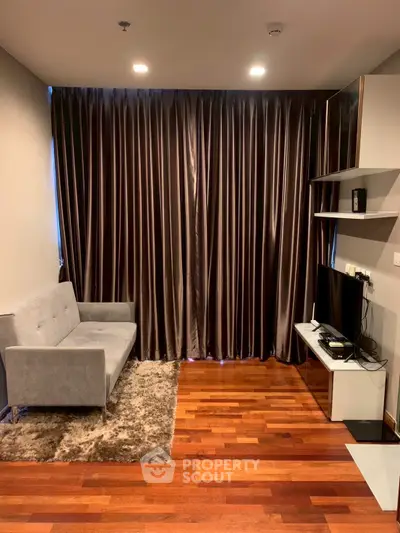 Modern living room with sleek gray sofa, TV setup, and elegant dark curtains on wooden flooring.