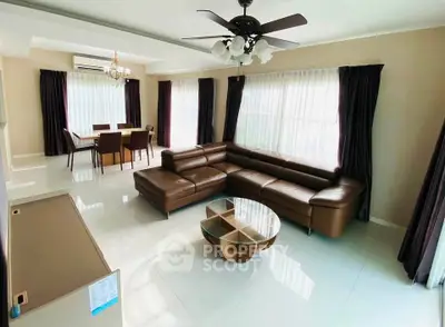 Spacious living room with elegant leather sofa and dining area, featuring large windows and modern ceiling fan.
