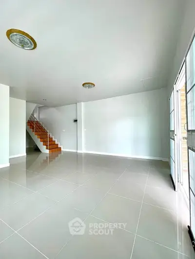 Spacious modern living room with sleek tile flooring and staircase, perfect for contemporary living.