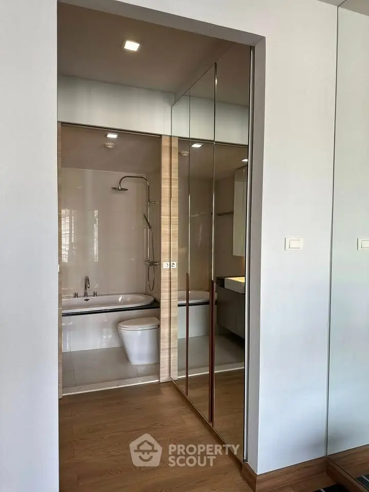 Modern bathroom with glass door and wooden flooring, featuring a sleek bathtub and shower.