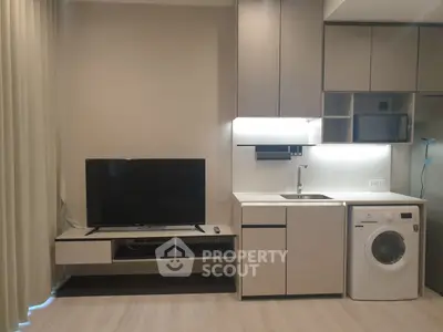 Modern living room with TV, washing machine, and sleek cabinetry in a compact space.