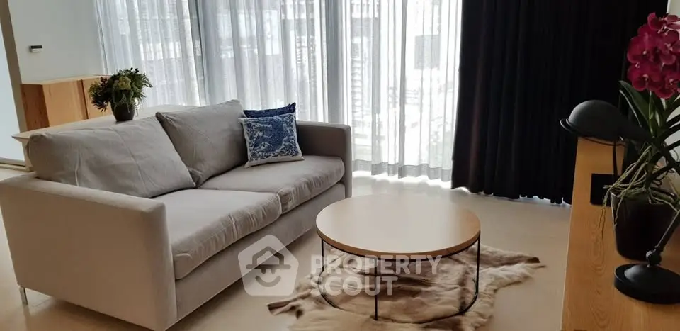 Modern living room with stylish sofa, round coffee table, and large windows with sheer curtains.