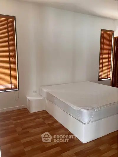 Spacious bedroom with wooden flooring and natural light from large windows with blinds.