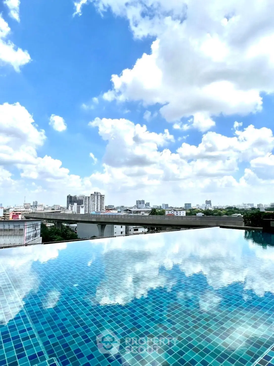 Stunning rooftop pool with panoramic city skyline view under a vibrant blue sky.