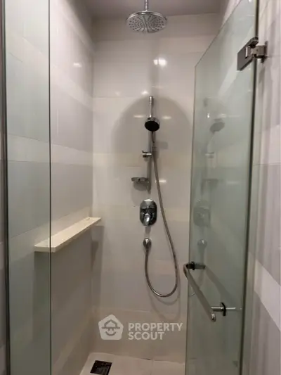 Modern shower area with glass door and rainfall showerhead in sleek bathroom.