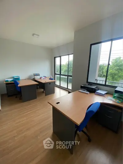 Spacious office room with large windows and modern desks, offering a serene view and ample natural light.