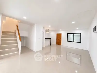 Spacious modern living room with glossy tile flooring and staircase, ideal for family gatherings.