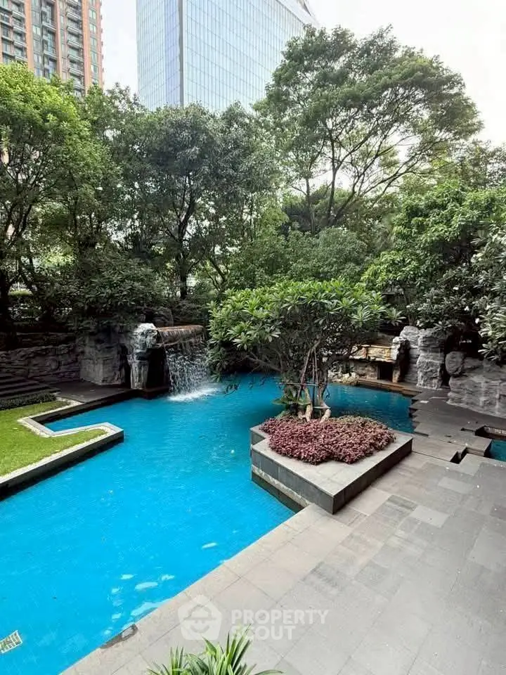 Luxurious outdoor pool area with lush greenery and waterfall feature in a modern residential complex.