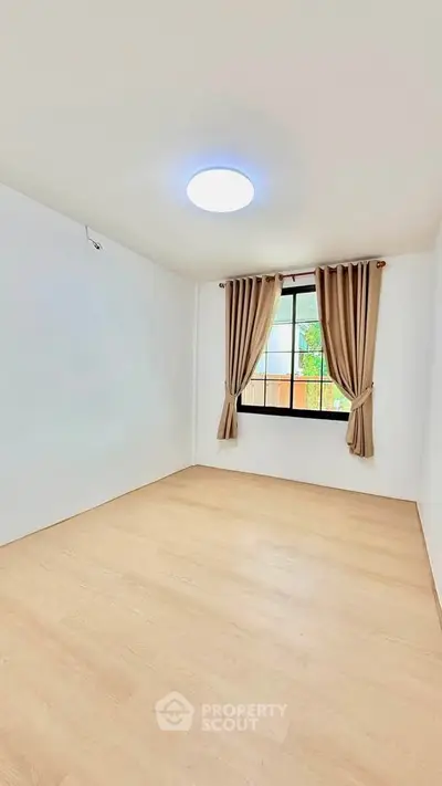 Spacious empty room with wooden flooring and large window with curtains, perfect for customization.