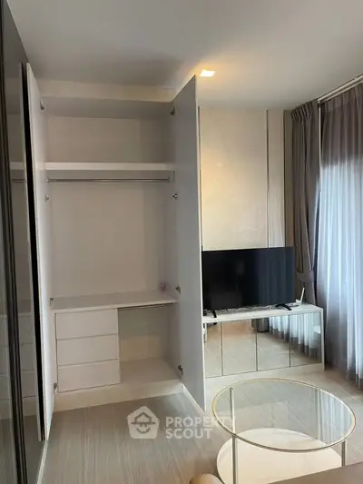 Modern living room with open closet and TV, featuring elegant curtains and a glass coffee table.