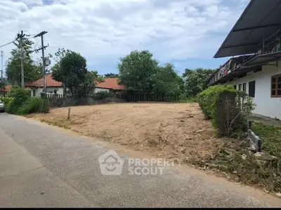 Expansive vacant land parcel ready for development, nestled in a serene neighborhood with lush greenery and clear skies.