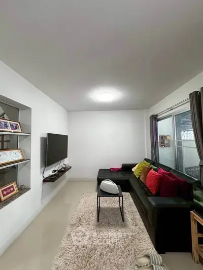 Modern living room with sleek black sofa and colorful cushions, featuring a wall-mounted TV and cozy rug.