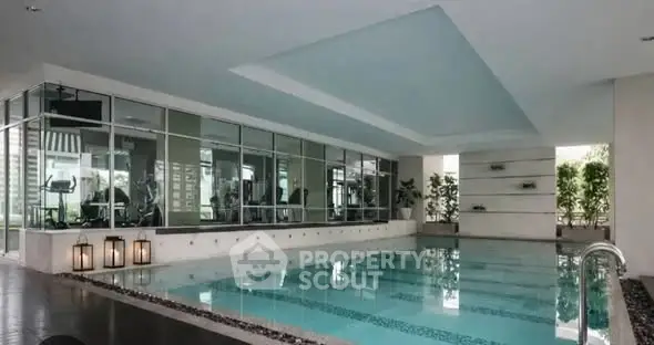 Luxurious indoor swimming pool with modern design and gym view in upscale residential building.