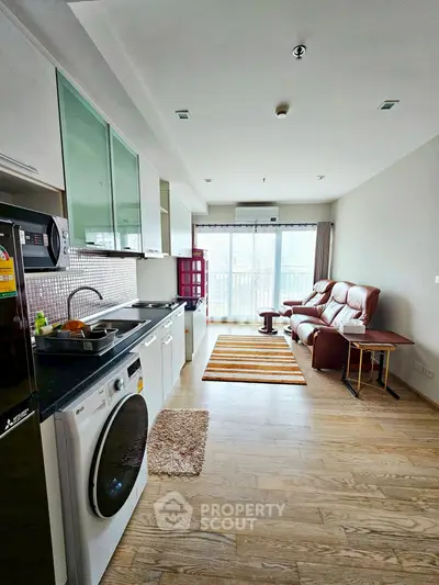 Modern open-layout living room with kitchen, featuring washing machine and cozy seating area.
