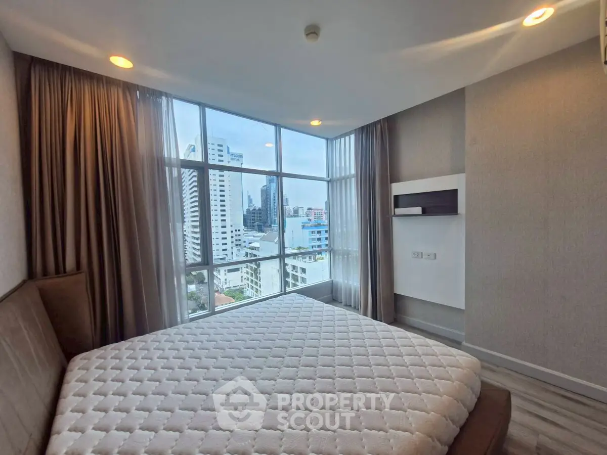 Modern bedroom with large windows offering stunning city views in a high-rise apartment.
