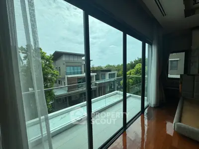 Modern balcony with glass doors offering serene views of contemporary homes and lush greenery.