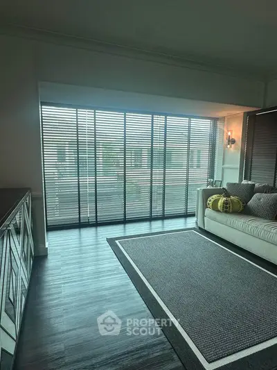 Spacious living room with large windows and modern decor, featuring a cozy sofa and elegant flooring.