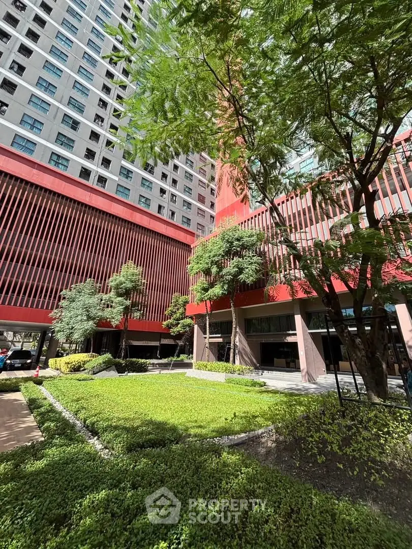 Modern building exterior with lush garden and tall trees, showcasing urban living.