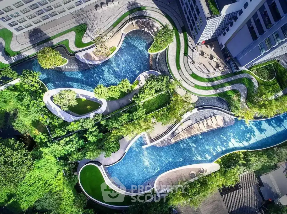 Stunning aerial view of luxury apartment complex with winding pool and lush greenery.