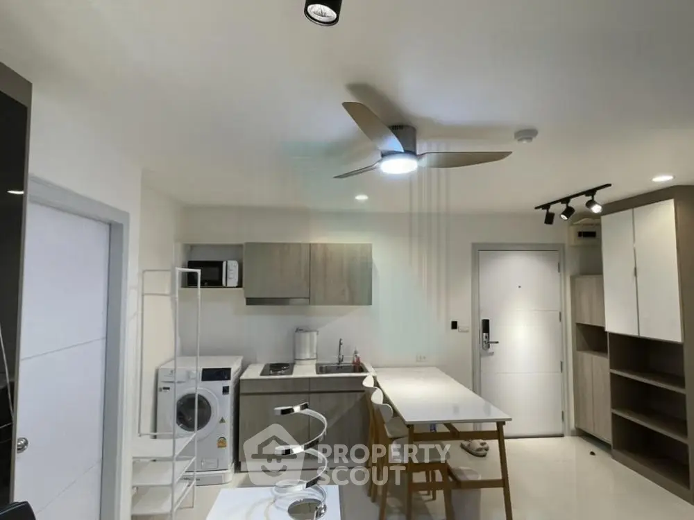 Modern kitchen with sleek cabinetry, dining area, and ceiling fan in a contemporary apartment.