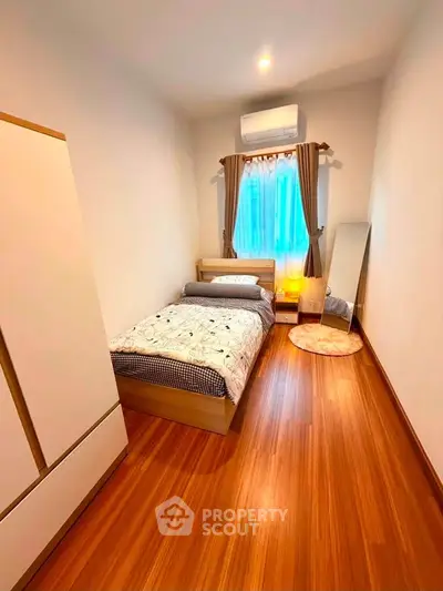 Cozy bedroom with wooden flooring, single bed, and natural light from window.