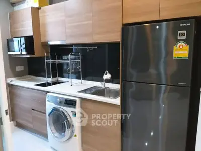Modern kitchen with sleek appliances and wooden cabinetry, featuring a washing machine and stainless steel fridge.