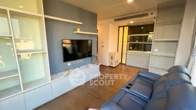 Modern living room with sleek built-in shelves and large TV, featuring a cozy blue sofa and wooden flooring.